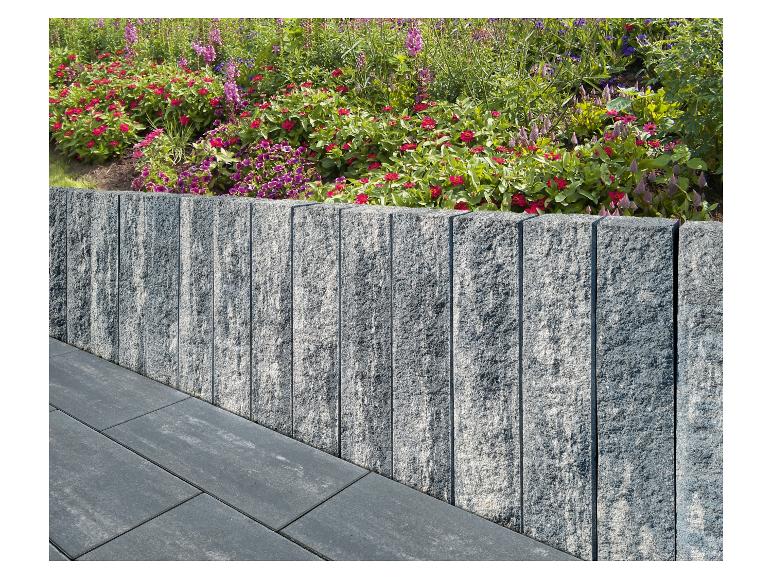 Steinmauer mit farbenfrohem Blumenbeet und Terrassenplatten.