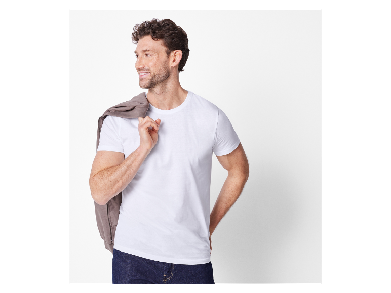 Lächelnder Mann in weißem T-Shirt mit brauner Jacke über der Schulter.