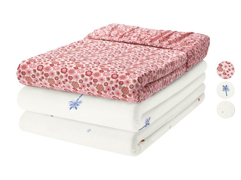 Rosa Blumenmuster und zwei weiße Kinderbettlaken mit Palmen- und Punktmustern.