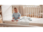 Lächelndes Baby in blauem Schlafanzug mit Eisbärmuster, sitzend in einem weißen Kinderbett neben einem passenden Schlafsack.