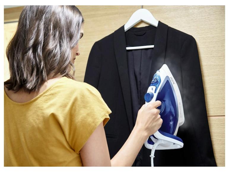 Frau dämpft eine schwarze Jacke mit einem Bügeleisen.
