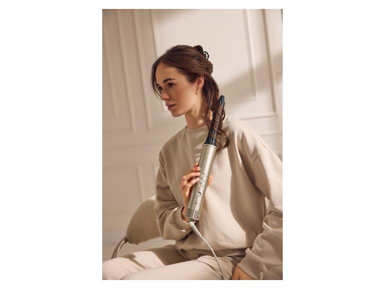 Frau hält eine Cien Warmluftbürste in ihren Haaren, trägt einen beigen Trainingsanzug.