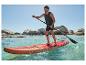 Mann auf rotem SUP-Board paddelt im Meer, mit Felsen im Hintergrund.