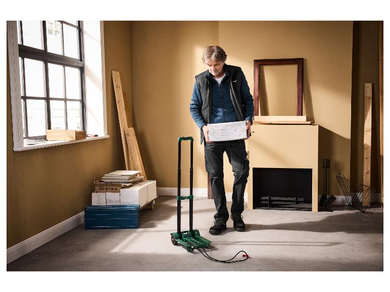 Mann hält Paket, mit Klappwagen und Baumaterialien in der Nähe.