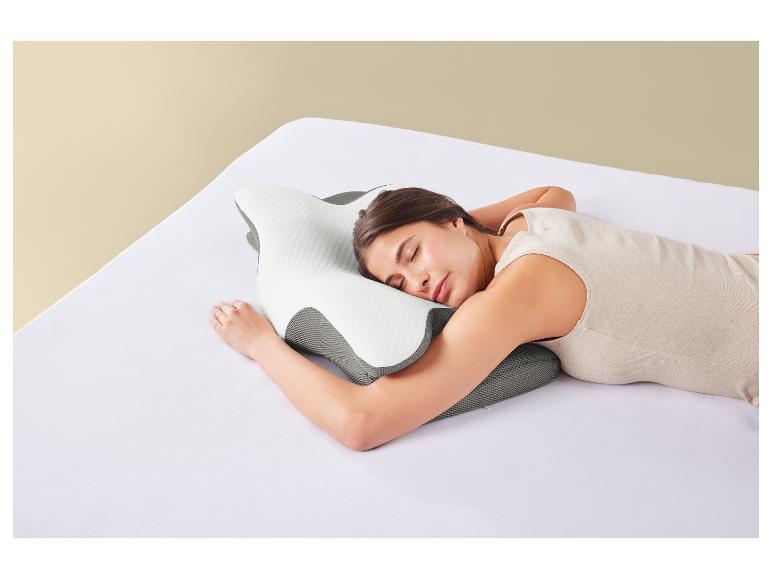 Eine Frau schläft auf einem orthopädischen Kissen auf einem weißen Bett.