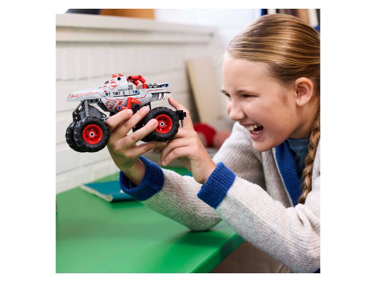 Glückliches Mädchen hält einen grau-roten LEGO Technic Monster Jam Thunderroarus Monstertruck.