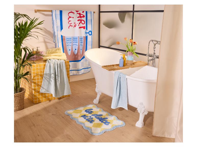 Badezimmer mit weißer Badewanne, gelben Fliesen, Pflanze und Handtüchern, mit einem Teppich „la dolce vita“.