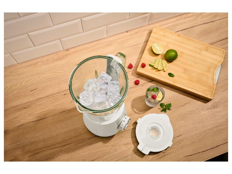 Mixer mit Eis, Limetten, Himbeeren und Minze auf einer Holzoberfläche.