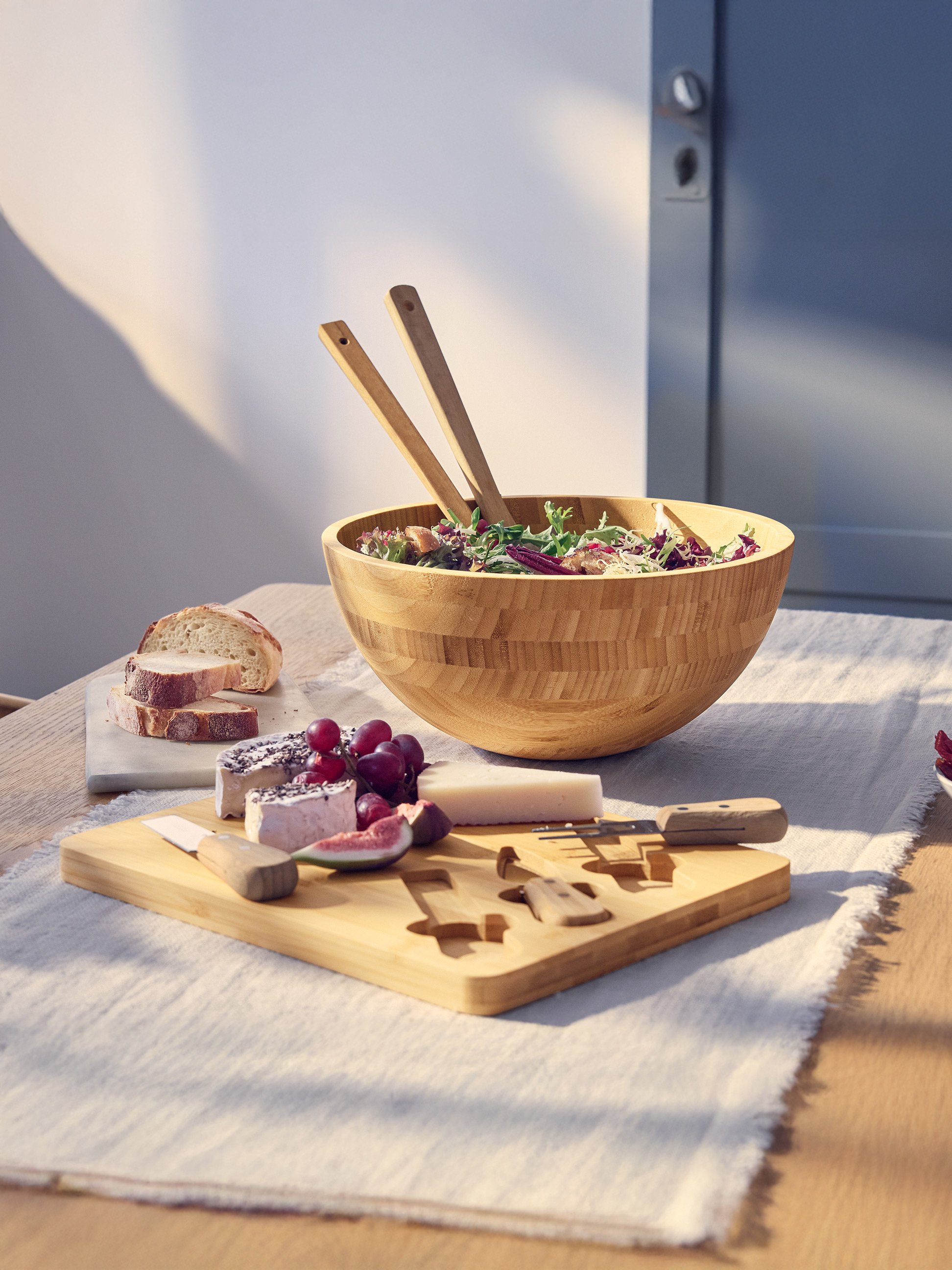 Salat in Holzschale mit Besteck, Käseplatte mit Brot und Obst.