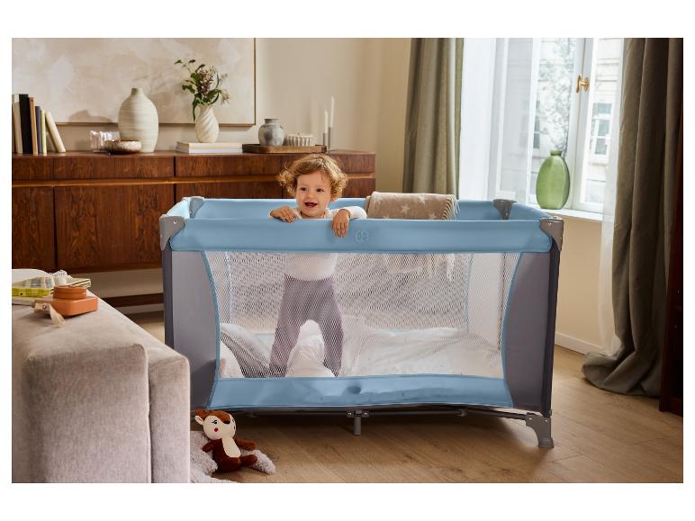 Baby in blauem Reisebett im Wohnzimmer.