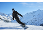Männlicher Snowboarder in schwarzem Anzug und Helm in den Bergen, umgeben von Schnee.