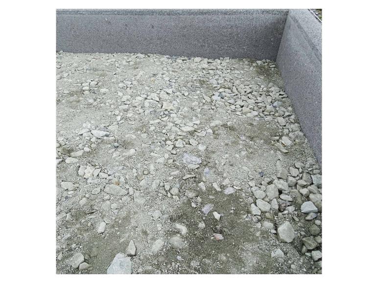 Boden mit Kies und Sand bedeckt, umgeben von Betonwänden.