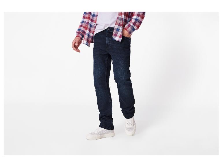 Mann trägt dunkelblaue Jeans, ein weißes T-Shirt und ein kariertes Hemd.