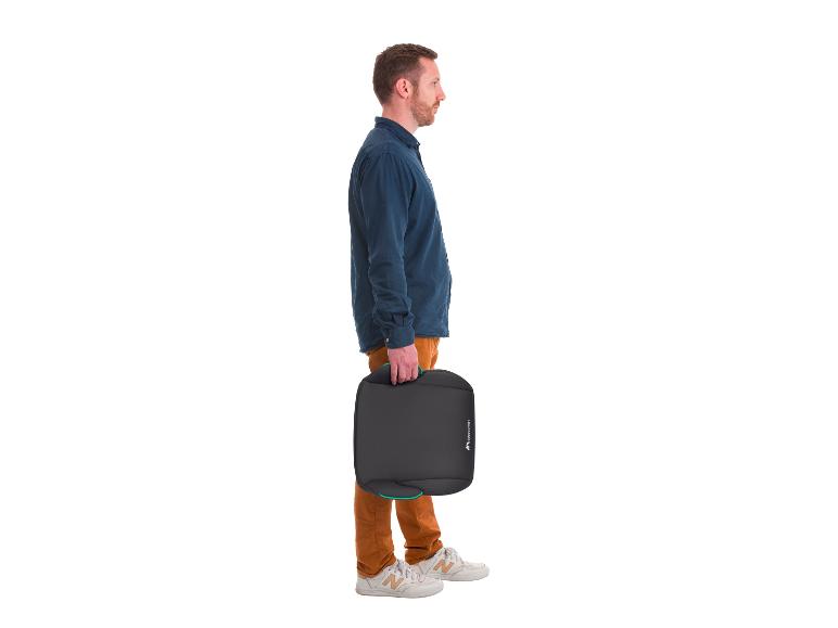 Mann in blauem Hemd und brauner Hose, der eine schwarze Babyschale hält.