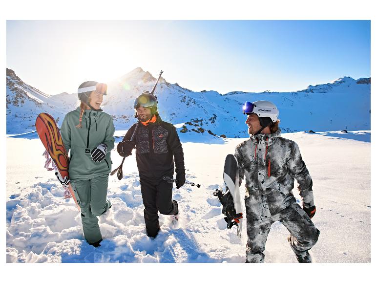 Eine Frau in grüner CRIVIT Freeride-Jacke mit Freunden auf einem verschneiten Berg.