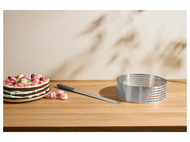 Kuchen mit Macarons, Tortenmesser und verstellbarer Tortenschneideform auf Holztisch.