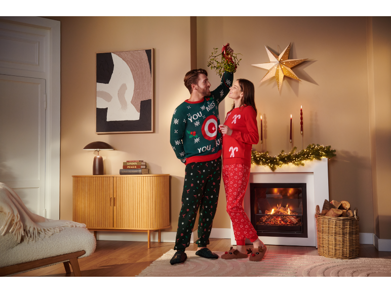 Ein Paar in festlichen Weihnachts-Pyjamas und Pullovern posiert unter einem Mistelzweig am Kamin.