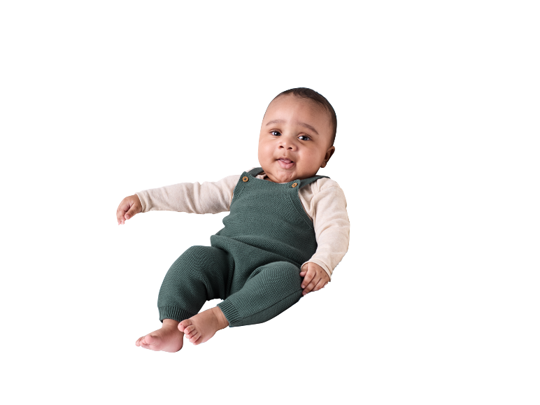 Baby in grünem Strickstrampler und cremefarbenem Langarmshirt