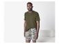 Mann in einem olivgrünen T-Shirt und gestreiften Boxershorts, stehend in einem Raum.