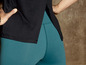 Eine Frau trägt ein schwarzes Oberteil und teal Leggings.