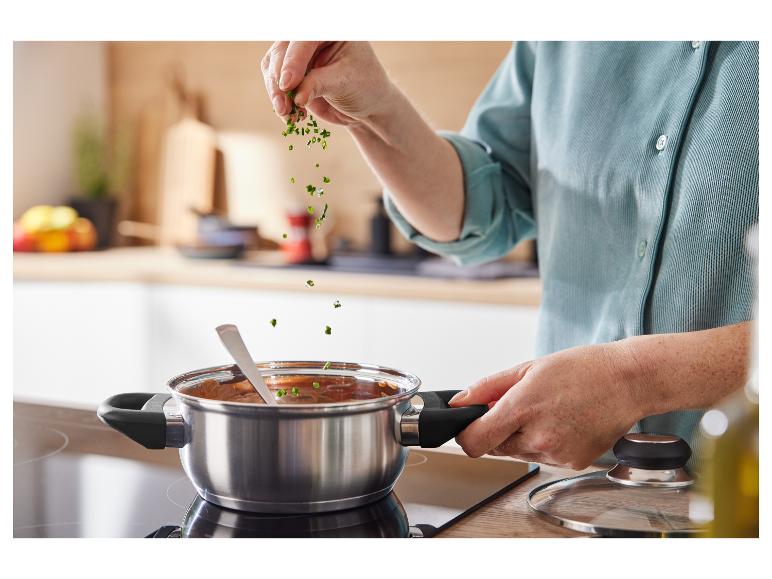 Eine Hand fügt frische Kräuter zu einem Topf auf einem Induktionskochfeld hinzu.