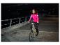 Frau in pinker Fahrradjacke fährt nachts ein E-Bike.