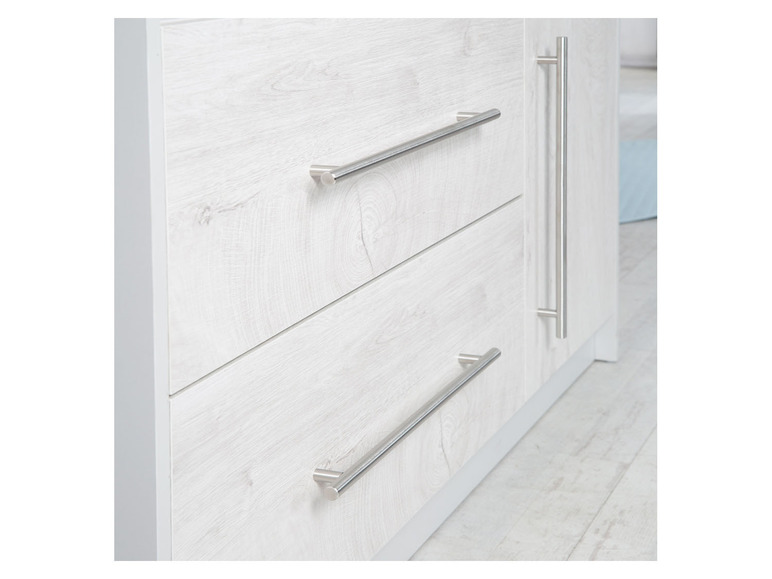 Ein weißer Schrank mit drei Schubladen und silbernen Griffen.