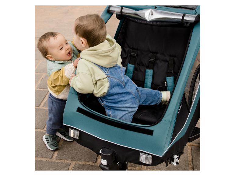 Zwei Kinder spielen in einem türkisfarbenen Hauck Dryk Duo Fahrradanhänger.