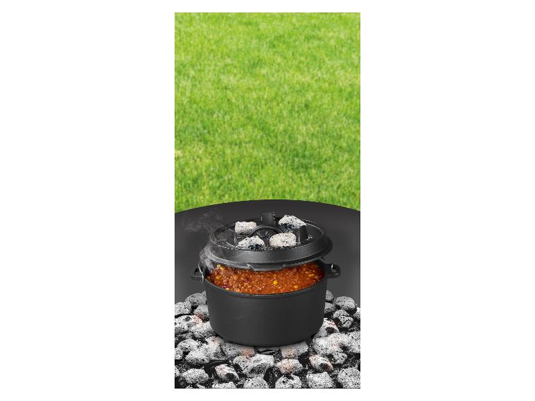 Gusseisen-Topf mit Essen, das auf Kohlen kocht, vor grünem Gras.