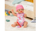 Babypuppe in rosa Strampler und Mütze, mit Schnuller, sitzt auf einem Teppich.