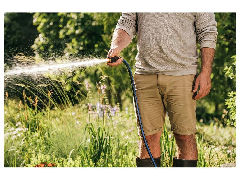 Mann bewässert Garten mit Gartenschlauch und Spritzpistole.