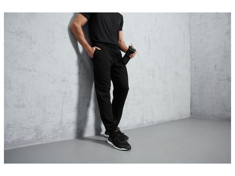 Ein Mann trägt schwarze Jogginghose, T-Shirt und Schuhe.