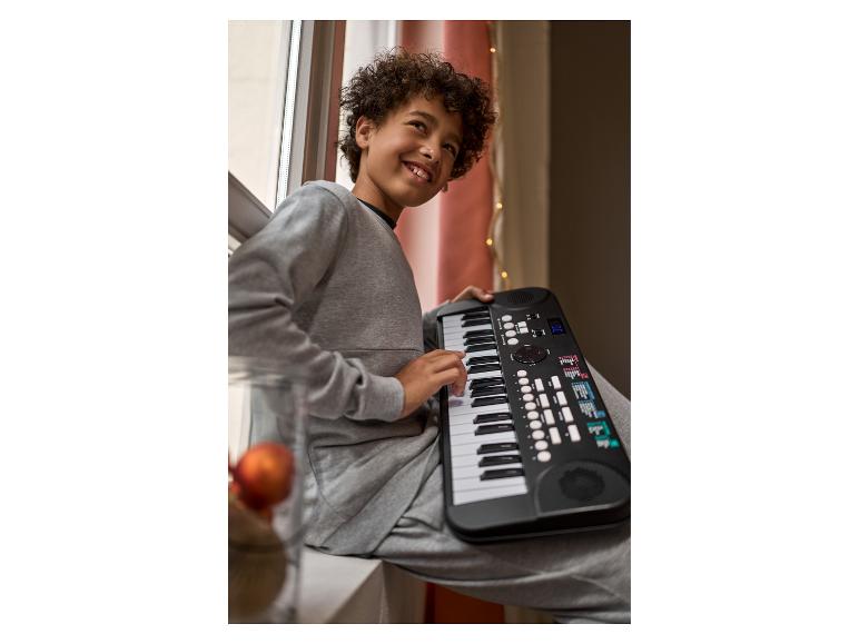 Junge sitzt am Fenster und spielt ein schwarzes elektronisches Klavier.