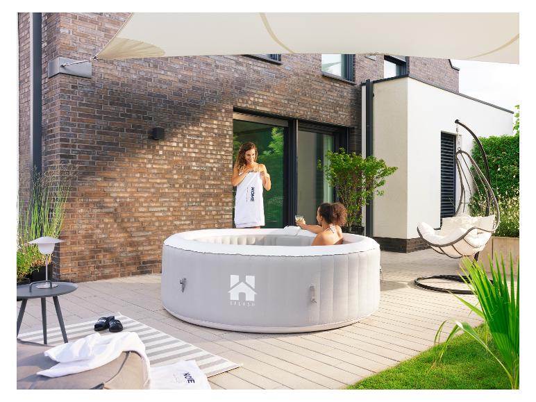 Zwei Frauen genießen einen grauen aufblasbaren Whirlpool auf einer Terrasse vor einem Backsteinhaus.