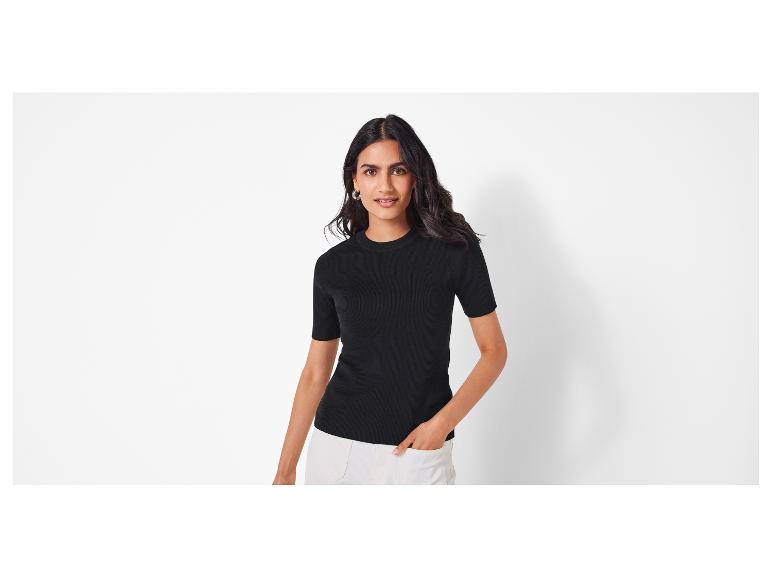 Frau in einem schwarzen T-Shirt mit kurzen Ärmeln und weißen Hosen.