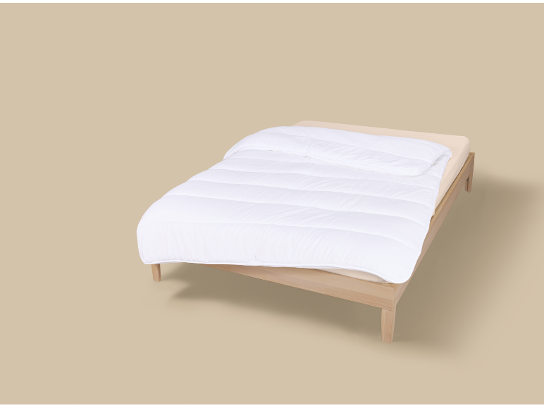 Einzelbett mit weißer Bettdecke und beigem Laken auf neutralem Hintergrund.