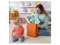 Eine Frau nimmt charakterförmige Babyspielzeuge aus einer orangefarbenen Geschenktüte, während ein Baby sie ansieht.