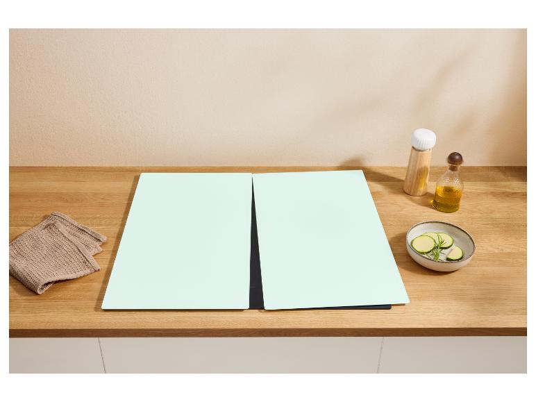 Zwei mintgrüne Schneidebretter auf einer Holztheke mit Handtuch, Öl und geschnittener Zucchini.