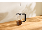 Wasser wird in eine French Press mit Kaffeepulver auf einer Holzoberfläche gegossen.