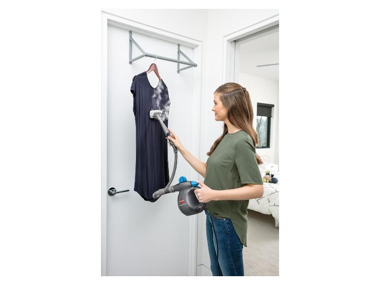 Frau glättet ein marineblaues Kleid mit einem Bissell Steam Shot Handdampfreiniger.