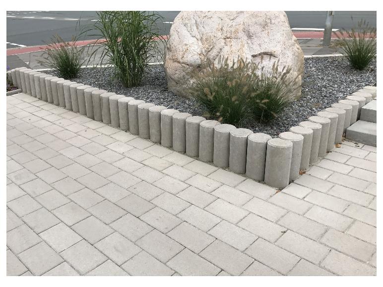 Gepflasterter Weg mit Betonrand und Kiesbeet mit Pflanzen und Stein.