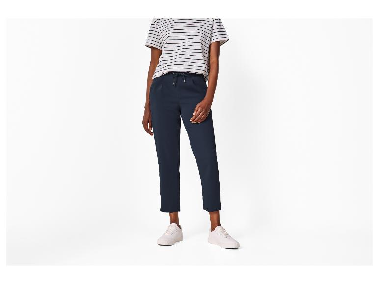 Frau in gestreiftem T-Shirt und dunkelblauer Hose mit weißen Sneakern.