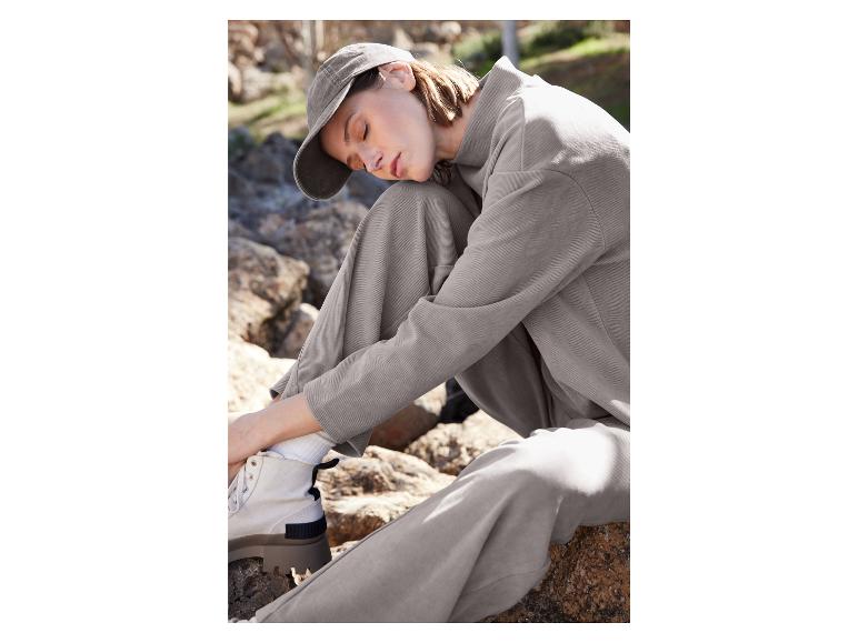 Frau in grauer Hose und grauem Pullover mit Kappe.