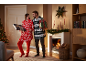 Ein Paar in festlichen Oversize-Hoodies mit Weihnachtsgeschenken am Kamin