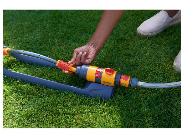 Eine Person schließt einen Gartenschlauch an einen Rasensprenger auf grünem Gras an.