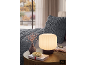 Nachttisch mit Lampe, Vase mit Trockenblumen, Schmuckschale und Buch neben einem Bett.