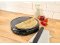 Crêpes-Maker mit Crêpes, Milch, Marmelade und Erdbeeren auf einer Holztheke.