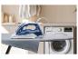 Dampfbügeleisen auf Bügelbrett mit Waschmaschine im Hintergrund.