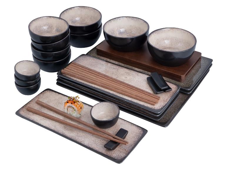 Ein Set schwarzer und beiger Schalen und flacher Teller mit Essstäbchen und Sushi.
