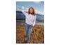 Frau in weißem Pullover und Jeans steht am Strand und blickt aufs Meer.